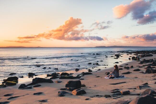 woman sitting on Noosa Beach at sunset Australia