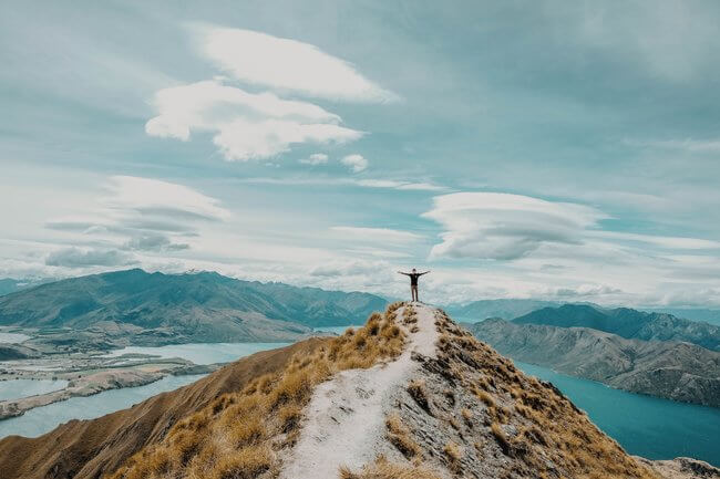 man standing on mountain top over lakes New Zealand