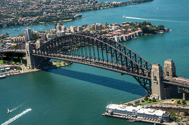 Sydney Harbour Bridge from above at day time, with calm emerald waters below