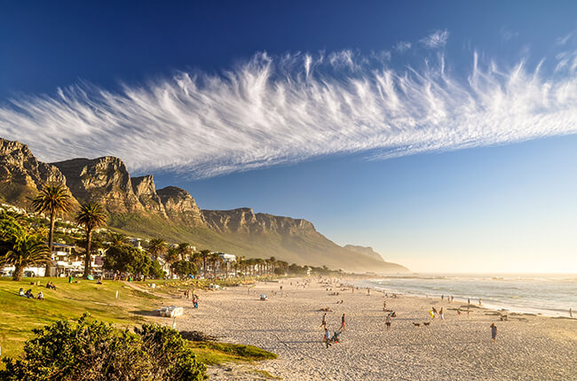 Cape Town beach at daytime, with wispy clouds interrupting the clear blue skies, and the Table mountains in the background