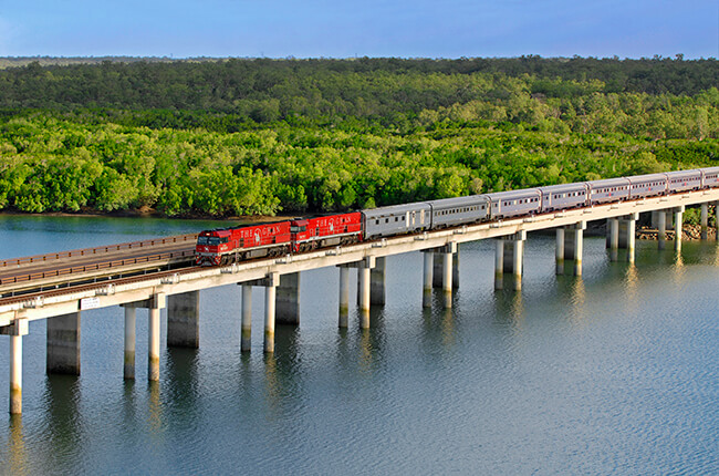 The Ghan train travelling over a bridge separating dense forest