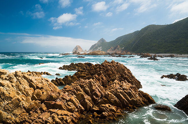 Jagged Rocks of Knysna in the white water, with green hills protecting the coast