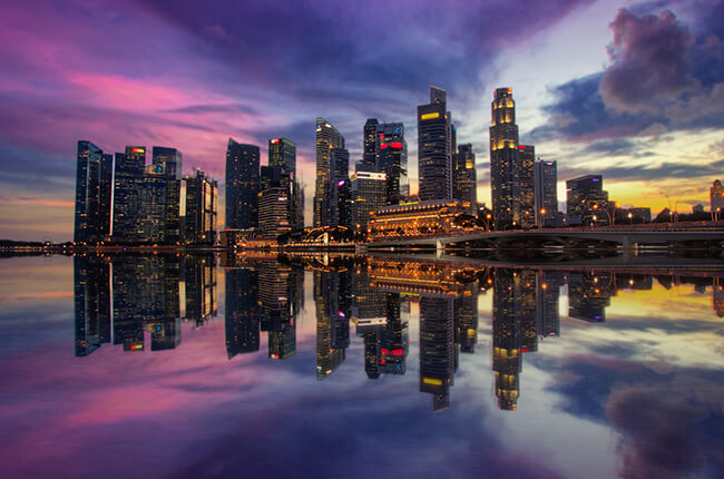 Singapore skyline reflected in the water of the Marina Bay, with streaks of purple in the sky