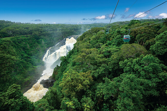 Cairns Skyrail travelling over dense rainforest, with strong waterfall flowing through a gorge