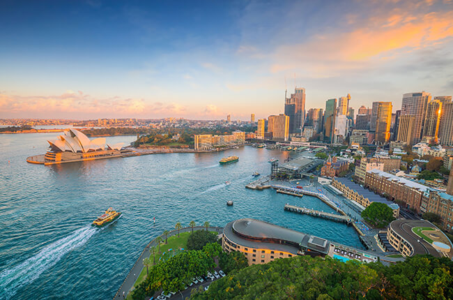 Aerial landscape of Sydney Opera House and city at sunset with boat cruises