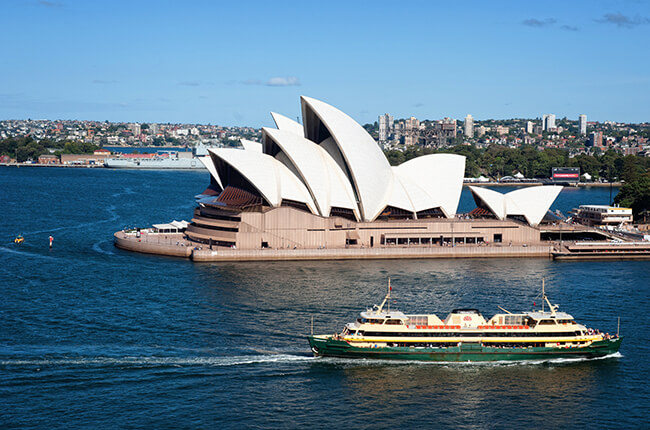 Sydney Opera House with blue water and cruise boat travelling past