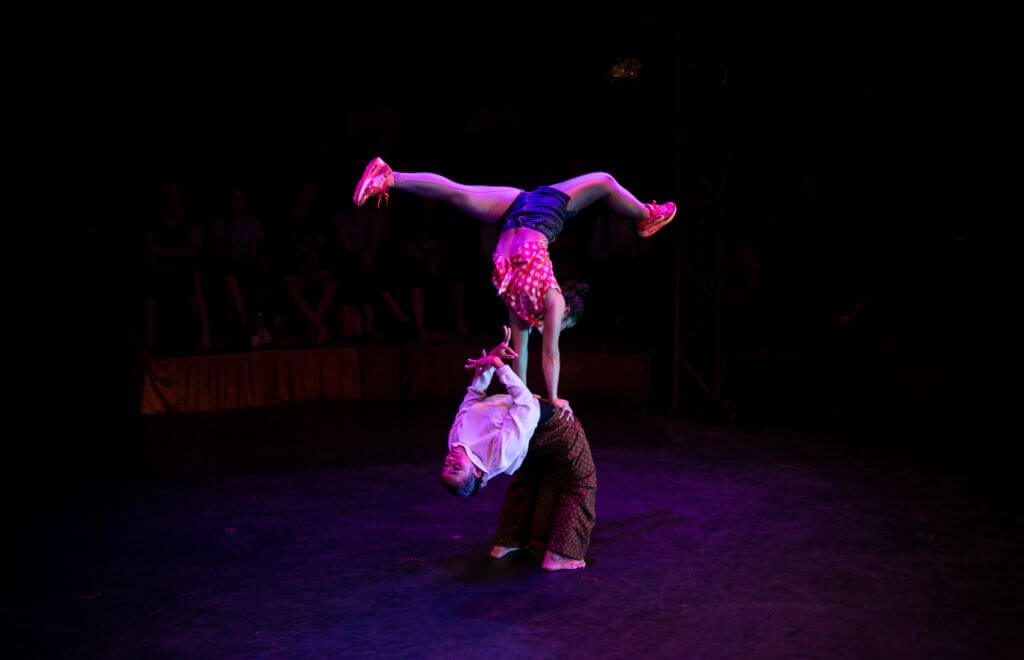 two acrobats one lay bent back and other upside down balancing on top