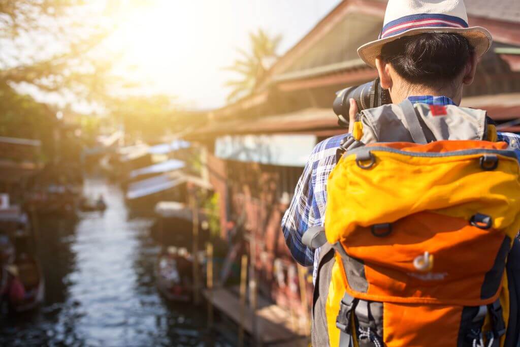 man in hat taking photo of river with houses