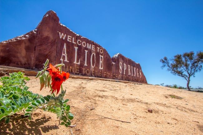 Alice Springs sign on rock at the top of a sand hill with blue skies
