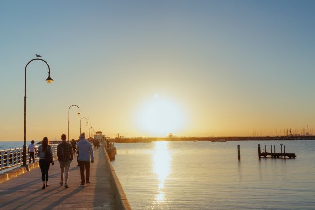 People walking along St Kilda pier, Melbourne. Sun low in the sky and reflecting on the sea
