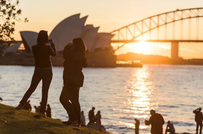 Sydney harbour at sunset with people in park and Opera House and Bridge in the background 