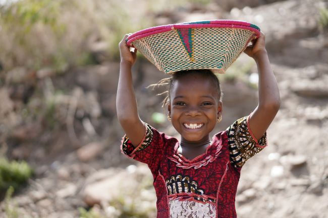 Local african child in traditional clothes with basket on her head