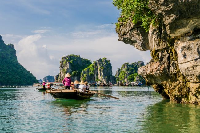 Tourists with local on small local boat admiring the views in Ha Long Bay, Vietnam