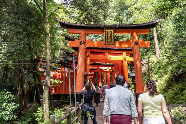 Tourists entering under the many Tori Gates of the Fushimi Inari Shrine, Kyoto, Japan