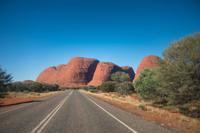 Open stretch of road towards Kaja Tjuta, (also known as The Olgas). The red rock stands out against a vivid blue sky