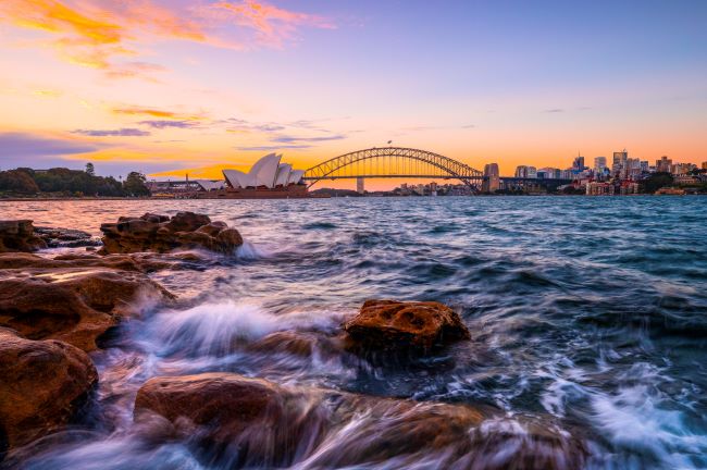 Sky of purples and oranges as sun sets over Sydney Harbour Bridge and Sydney Opera House