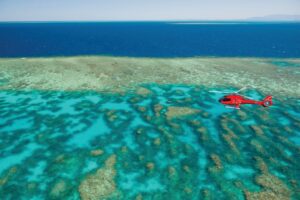 Red helicopter flying over the vivid blues on the Great Barrier Reef off the coast of Cairns in Australia