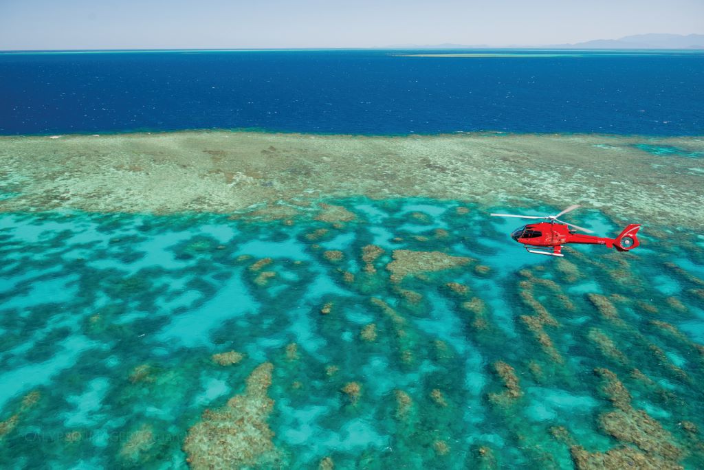 Red helicopter flying over the vivid blues on the Great Barrier Reef off the coast of Cairns in Australia