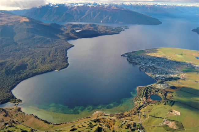 Aerial of the township of Te Anau, sitting on the shores of Lake Te Anau, with mountain range in the background