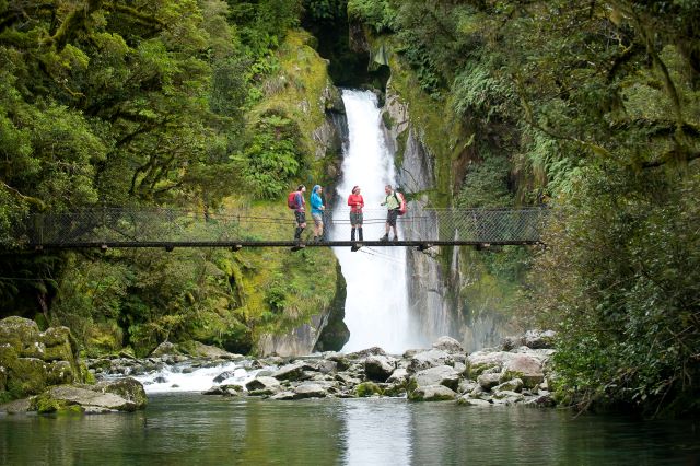 People standing on suspension bridge in front of the Giant Gate Waterfall on the Milford Track in Fiordland, New Zealand