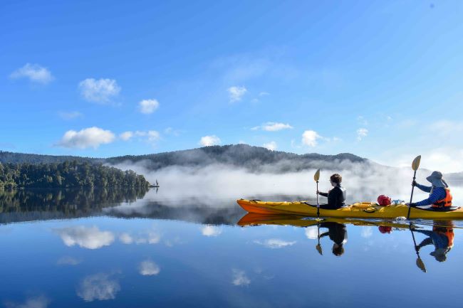 Couple kayaking on the blue waters of Lake Mapourika near Franz Josef on New Zealand's stunning West Coast