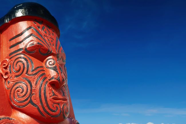 Close up of a traditional wooden Maori sculpture against a bright blue sky