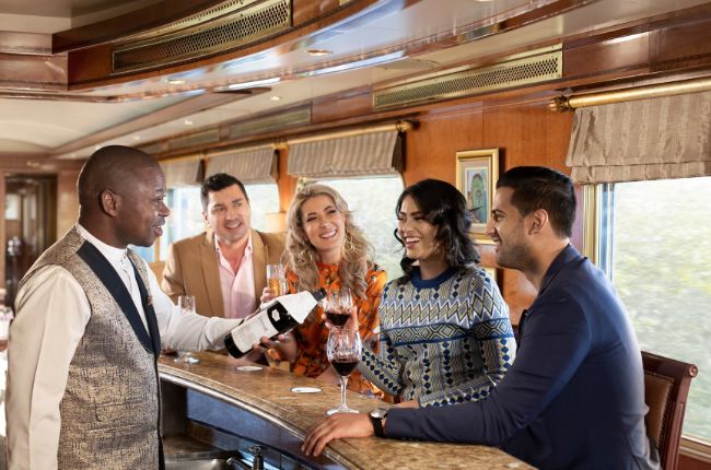 Butler pouring wine for guests aboard the blue train