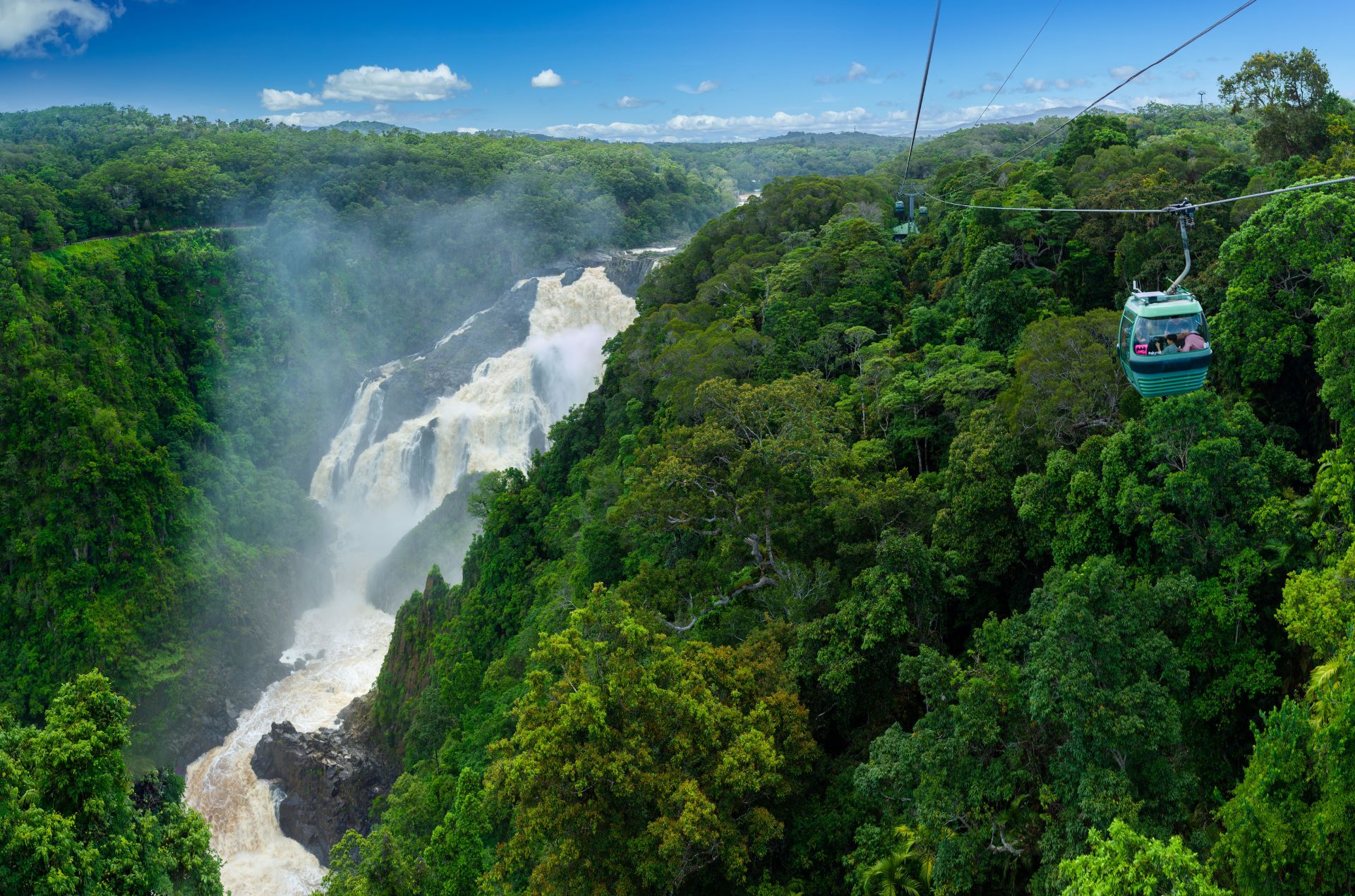 Cable car travelling high over the rainforst canpoy with waterfall in the background