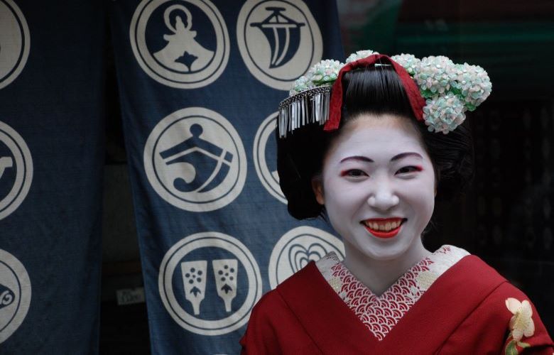 Laughing Maiko (apprentice Geisha) in traditional red kimono, white face and red lips