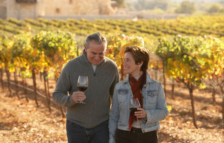 Couple with glasses of wine walking through a vineyard