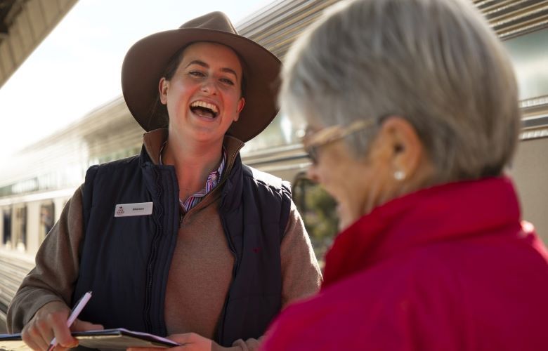 Ghan staff and lady tourist laughing together outside the train