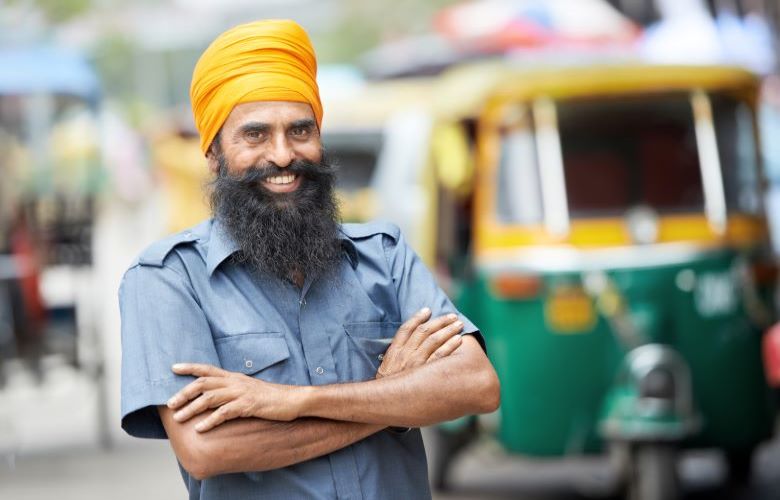 Smiling Indian man in front of green and yellow tuk-tuk