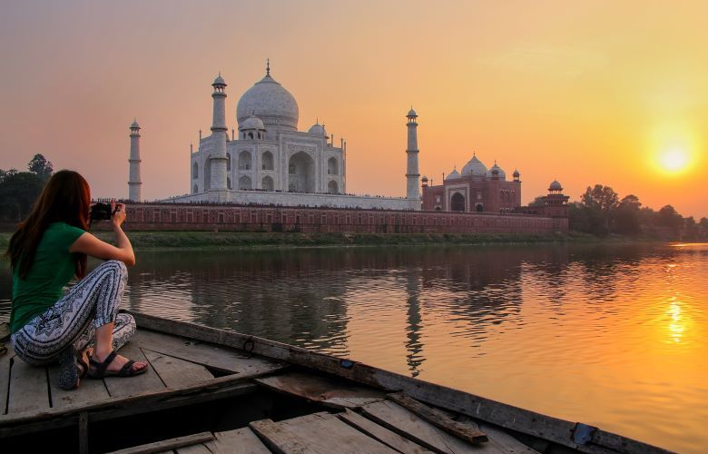 Woman sitting on a boat in front of the Tah Mahal taking a photograph at sunrise